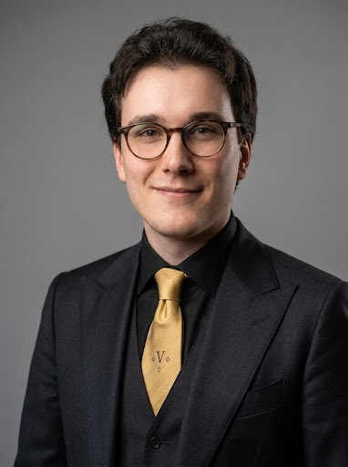 Official high-resolution portrait of Vincent Vegas in a charcoal suit and gold tie.